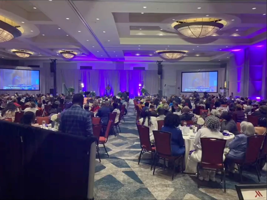 Conference ballroom with round-table seating, two projection screens, and purple stage lighting.